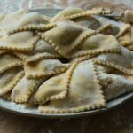 Ravioli freschi fatti in casa con ripieno cremoso di ricotta e spinaci su un tavolo di legno.